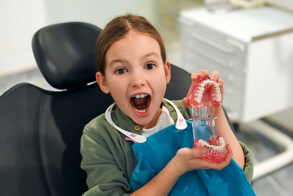 niña en el dentista con la boca abierta y mostrando unas dentaduras